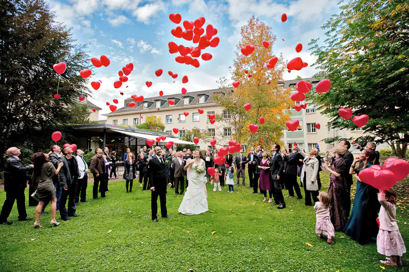 Hochzeitsfotografie von einem Brautpaar, dass mit Gästen rote Ballone steigen lässt. Hochzeitsfoto von UNIKATUM